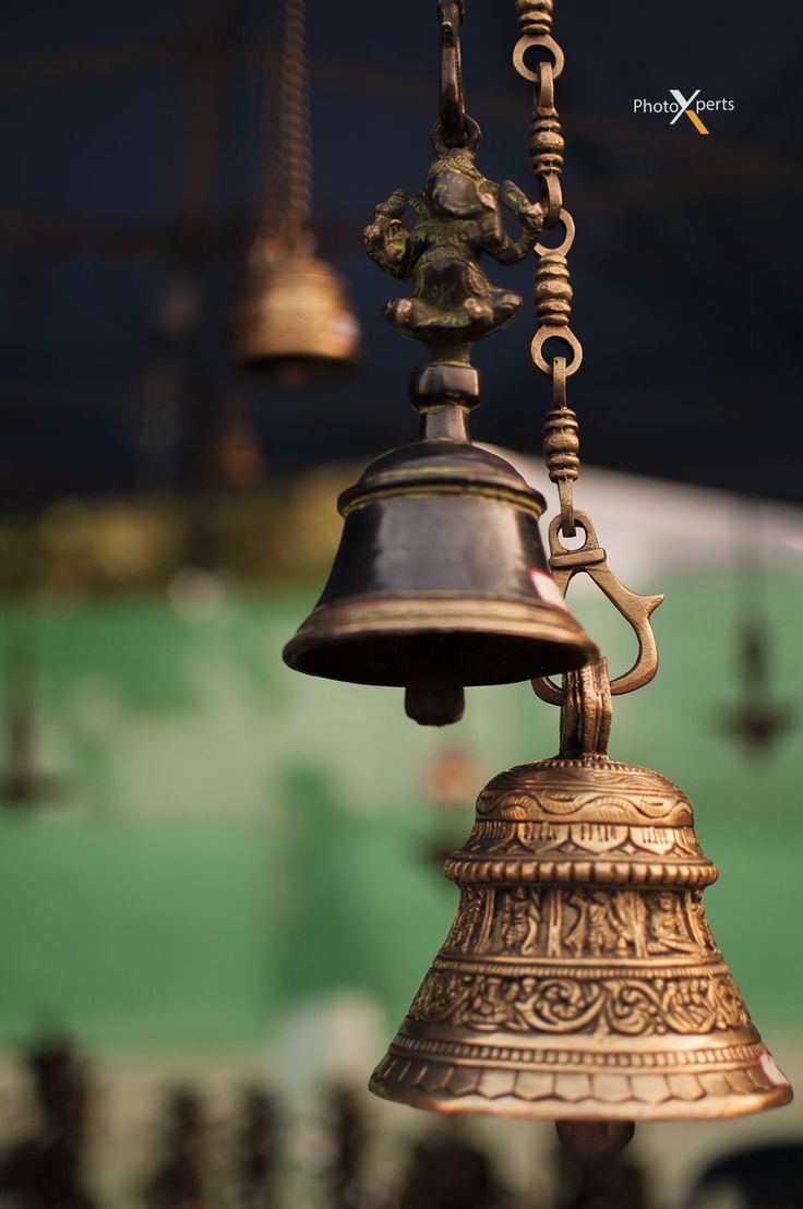 an old brass bell hanging from a chain in front of a green wall with other bells