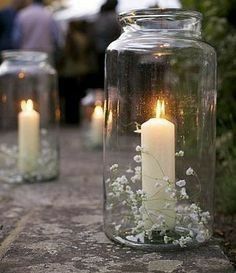 two glass jars filled with white flowers and lit candles are sitting on a stone path