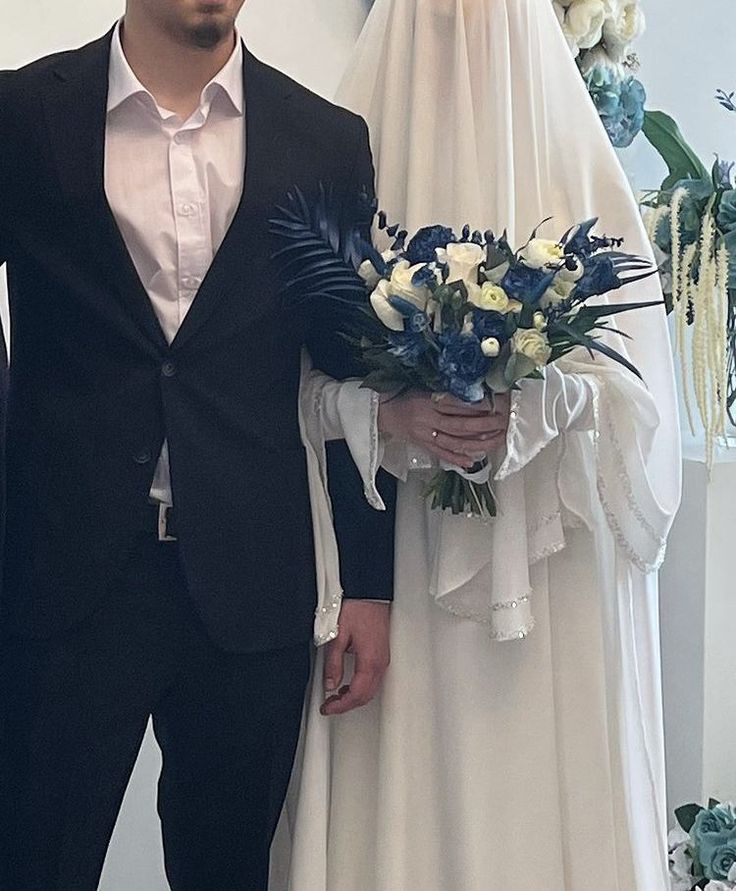 a man and woman dressed up in wedding attire standing next to each other holding bouquets