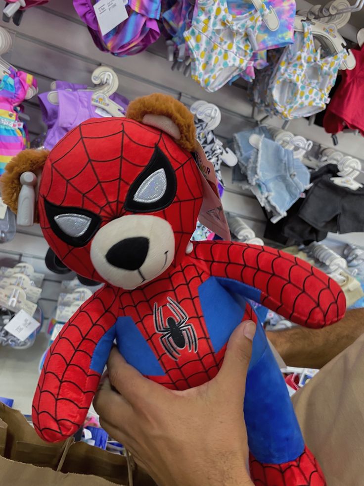 a spider man stuffed animal being held by someone's hand in front of a store display