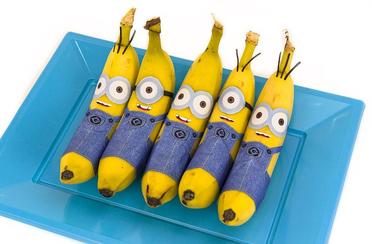 five bananas with faces drawn on them sitting on a blue plate next to some banana peels