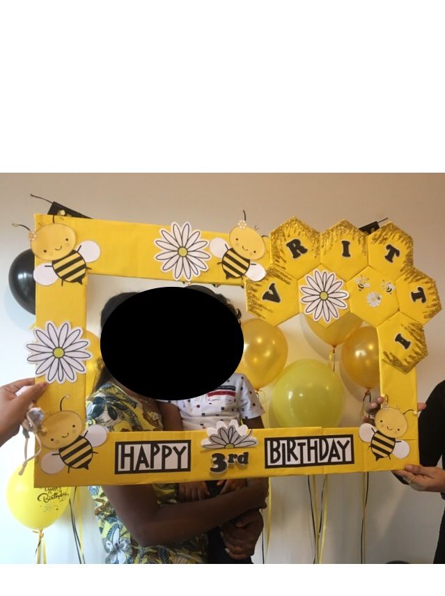 two people holding up a yellow frame with bees on it and balloons in the shape of honeycombs