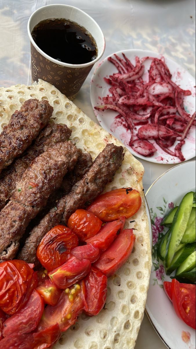 a plate with meat, tomatoes and cucumbers next to a cup of coffee