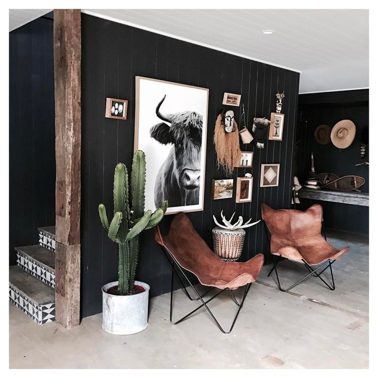 a living room with black walls and pictures on the wall next to two brown chairs