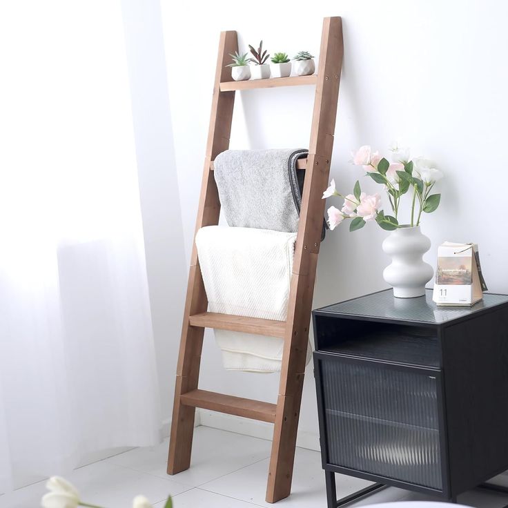 a wooden ladder leaning up against a wall next to a table with flowers on it