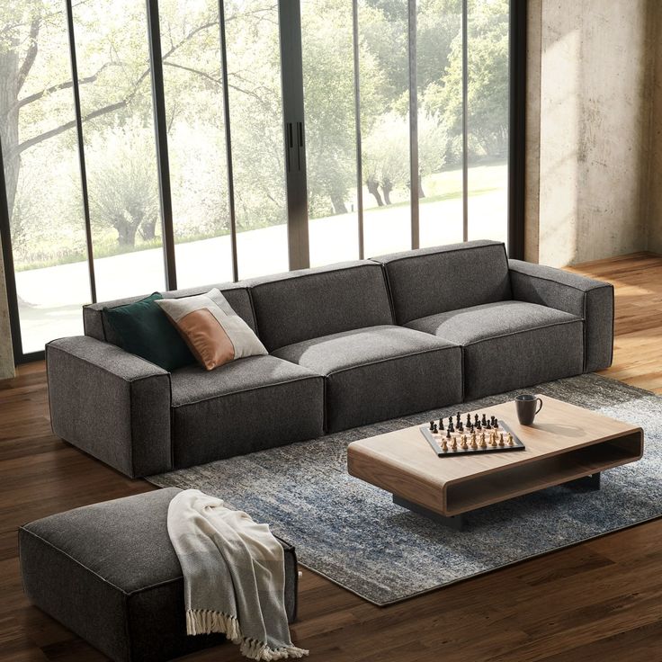 a living room with a couch, coffee table and chess board on the floor in front of large windows