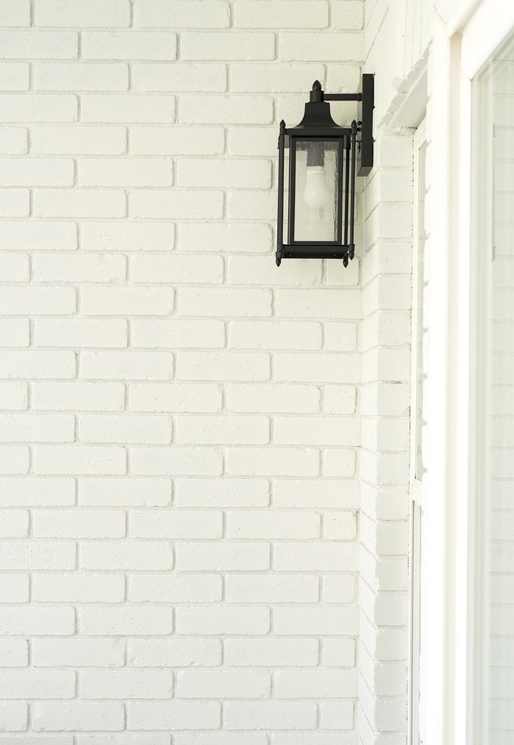 a white brick wall with a black lantern on the corner and a door in the background