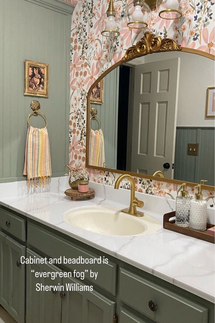 a bathroom with green cabinets and floral wallpaper on the walls, along with a gold faucet