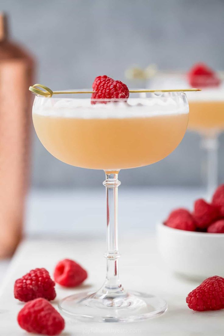 two glasses filled with champagne and raspberries on top of a white countertop