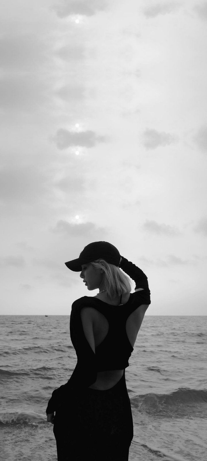 a woman standing on top of a sandy beach next to the ocean in black and white