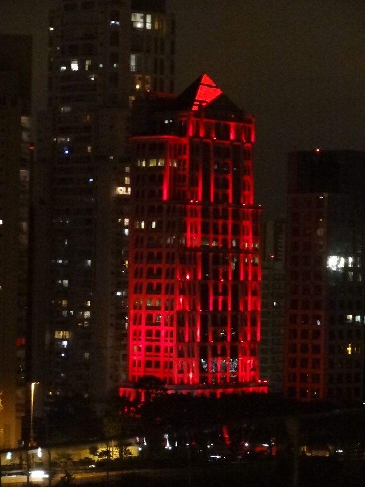 a tall building with red lights on it's side in the city at night