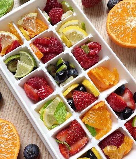 an ice tray filled with fruit and mint garnish on top of a wooden table