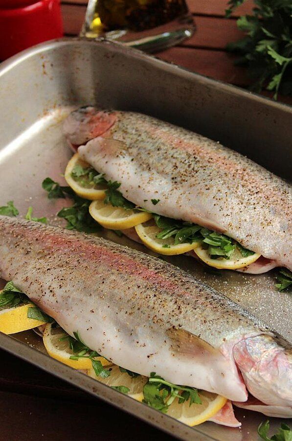 two fish in a pan with lemon slices and parsley