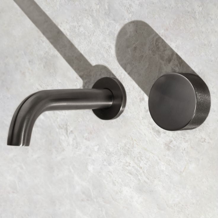 two black faucets on a white marble counter top with shadows from the wall behind them