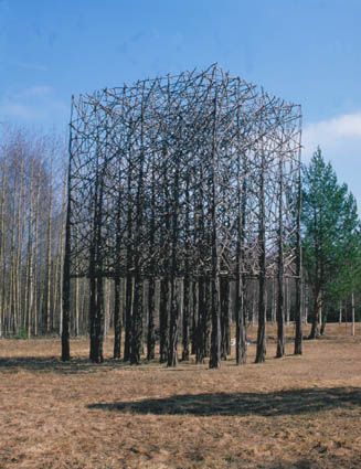 a sculpture in the middle of a field with trees around it and blue sky above