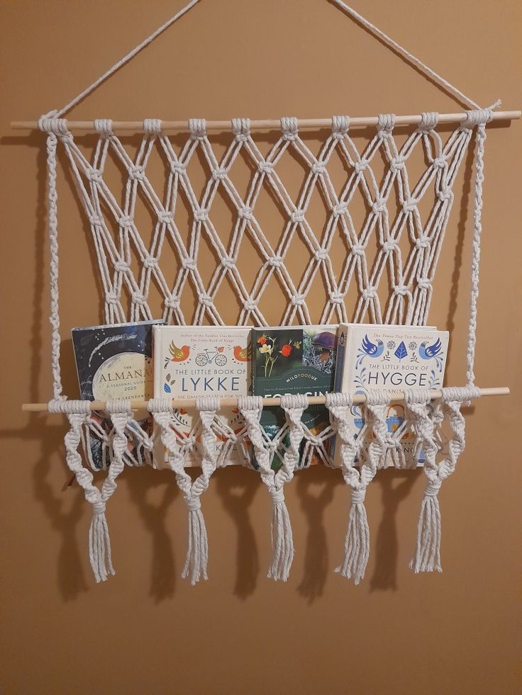 there is a macrame hanging on the wall with books in it and some tassels