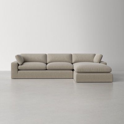 a beige sectional sofa with pillows on the top and bottom, in front of a white wall