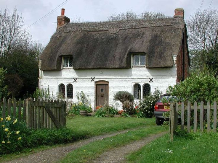 a car parked in front of a white house with a thatched roof and windows