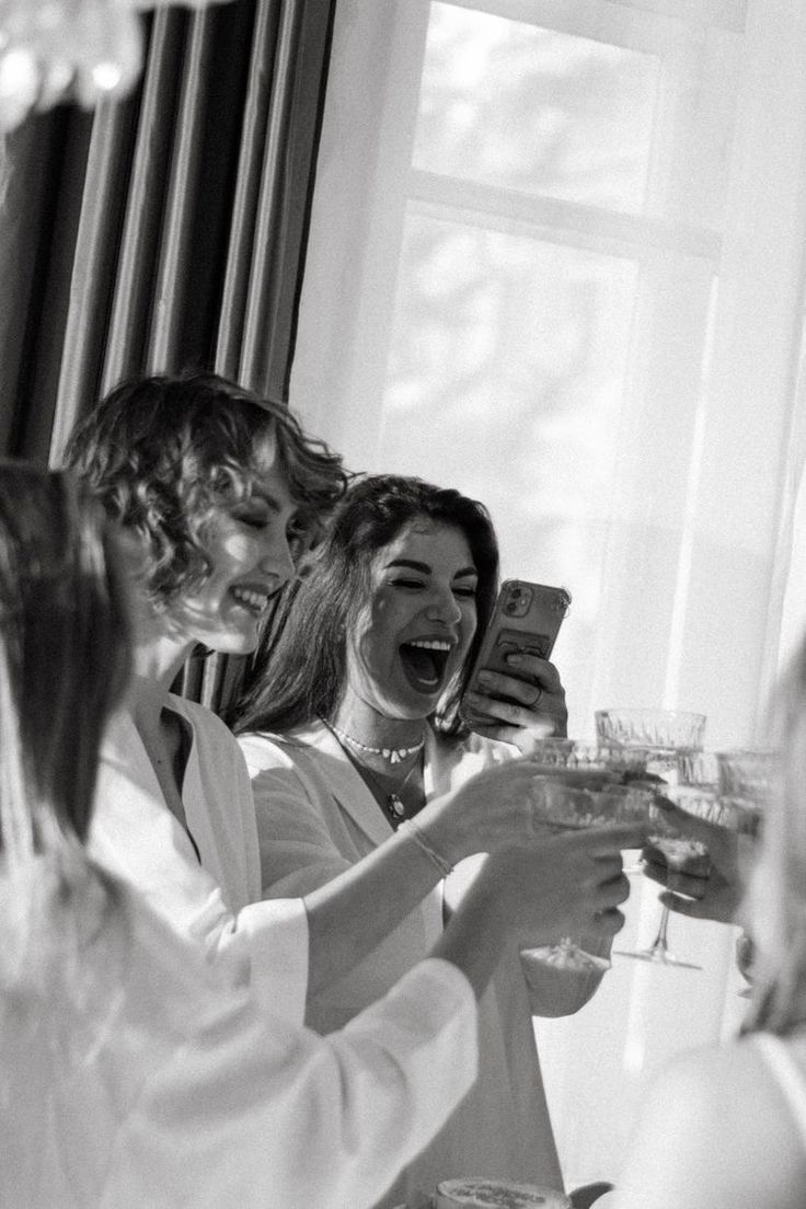 black and white photograph of three women laughing at each other while holding wine glasses in their hands