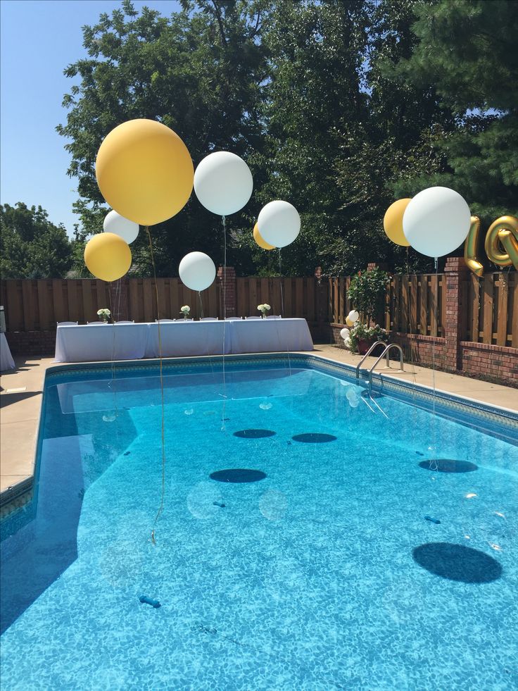 some balloons floating in the air near a swimming pool with blue water and yellow and white decorations