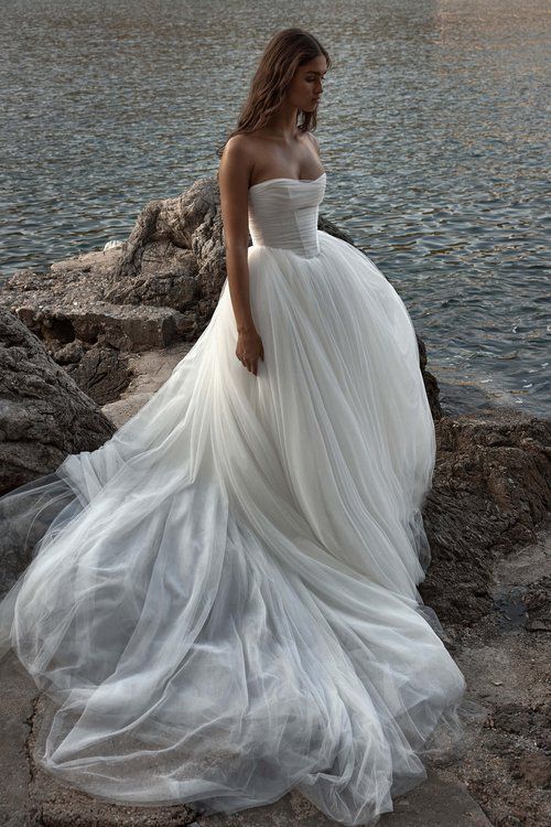 a woman in a white dress standing on rocks by the water with her hands behind her back