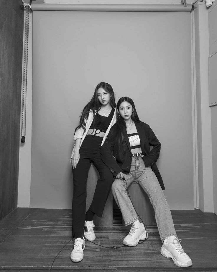 two young women sitting on the floor in front of a wall with a clock above them