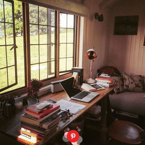 a laptop computer sitting on top of a wooden desk in front of two large windows