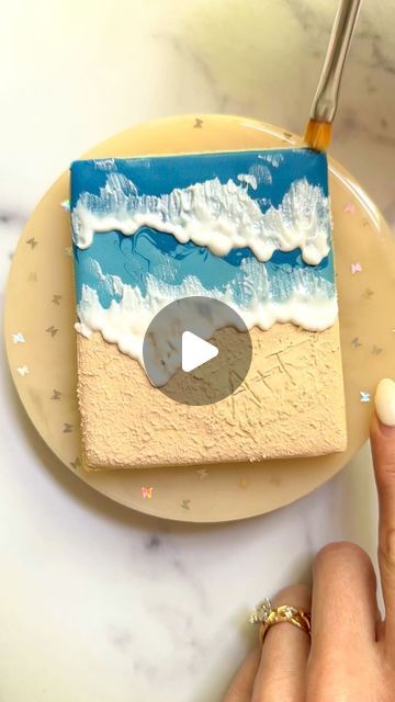 a person is painting a beach scene on a cake with icing and sprinkles