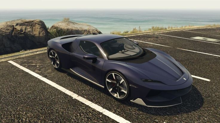 a blue sports car is parked in a parking lot next to the ocean and rocks