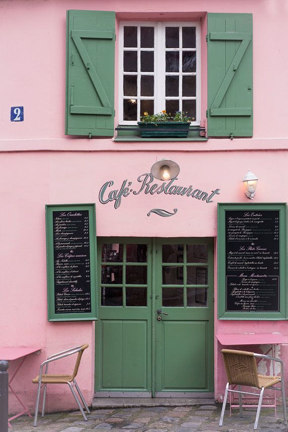 a pink building with green shutters and two chairs in front of the door that says cafe restaurant