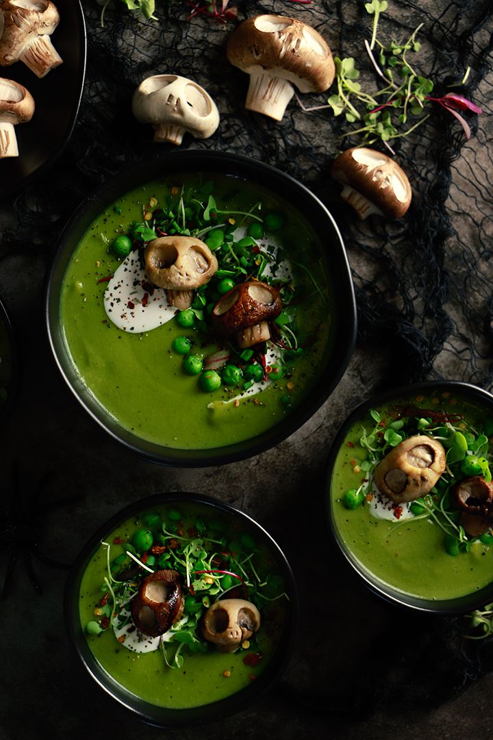 three bowls filled with green soup next to mushrooms and other vegetables on a black surface