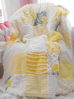 a yellow and white blanket sitting on top of a bed next to a pink flower