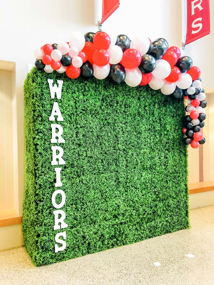 a wall made out of grass and balloons with the word warriors on it in white letters