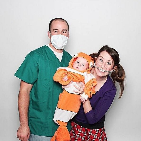 a man and woman wearing masks while holding a baby