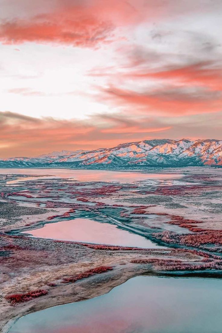 an aerial view of the mountains and lakes at sunset with pink hues in the sky