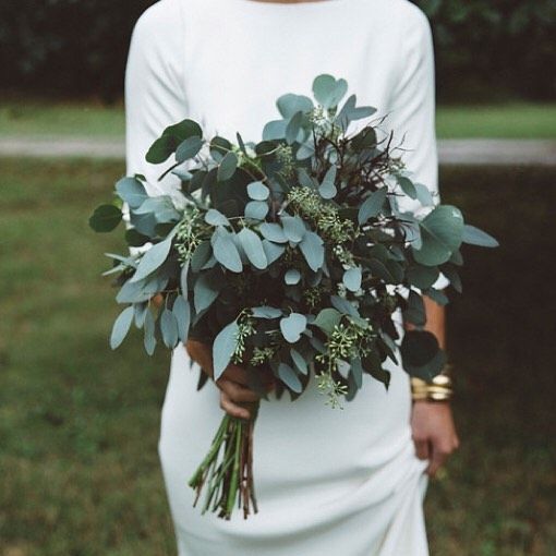 a woman in a white dress holding a bouquet of greenery