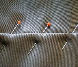 several pins are lined up on the side of a piece of fabric, with two orange ones in between them