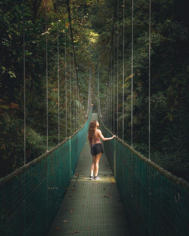 a woman walking across a suspension bridge in the forest with her arms out to the side