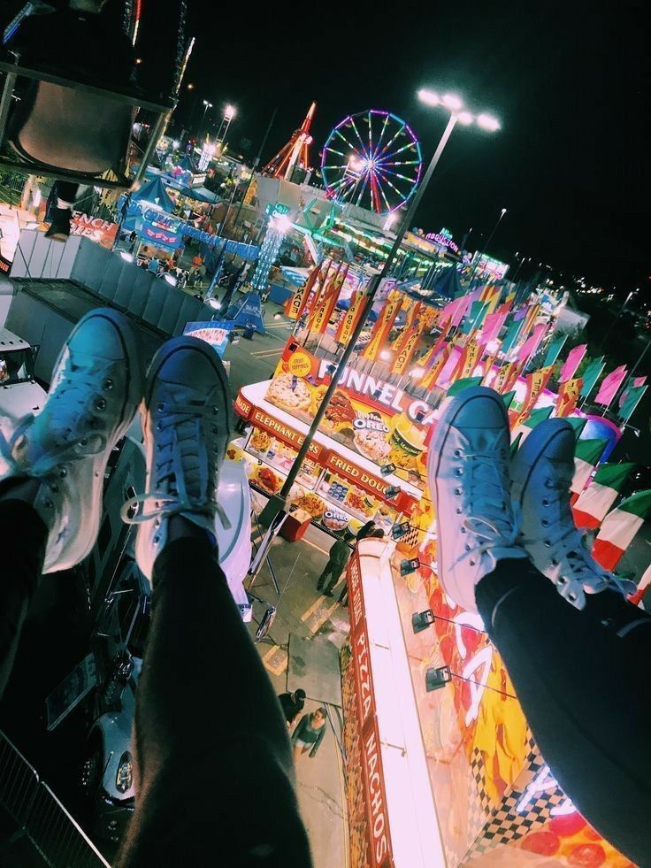 two people standing on top of skateboards in front of an amusement park at night