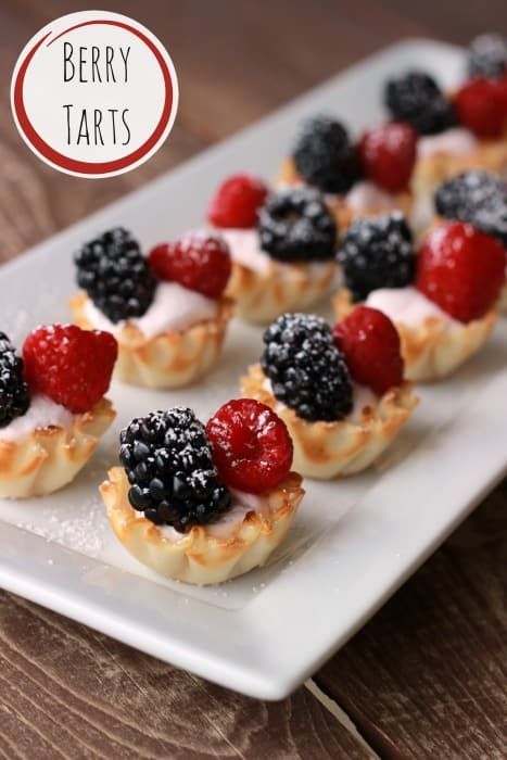 berry tarts with cream and blackberries on a white plate next to a wooden table