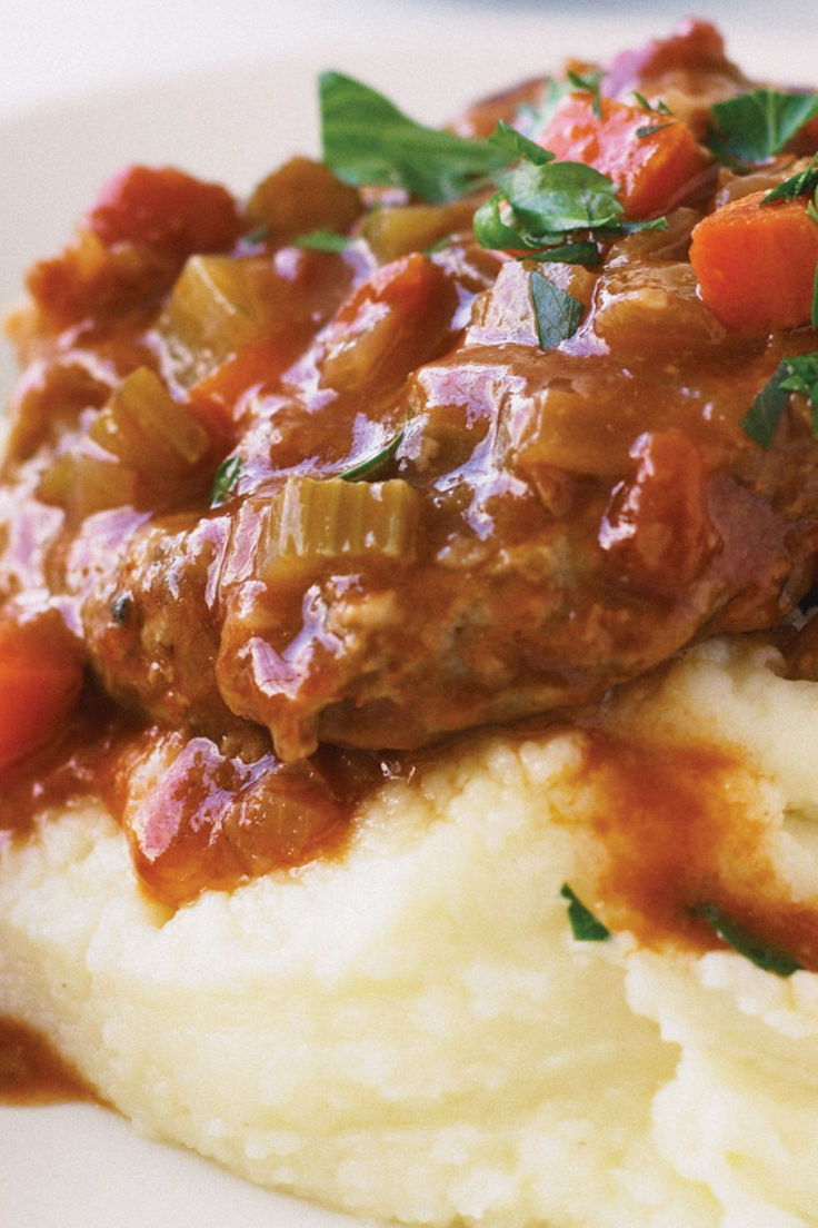 mashed potatoes topped with meat and vegetables in gravy on a white plate