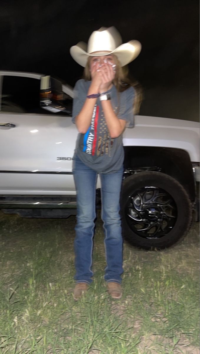 a woman standing in front of a truck talking on a cell phone while wearing a cowboy hat