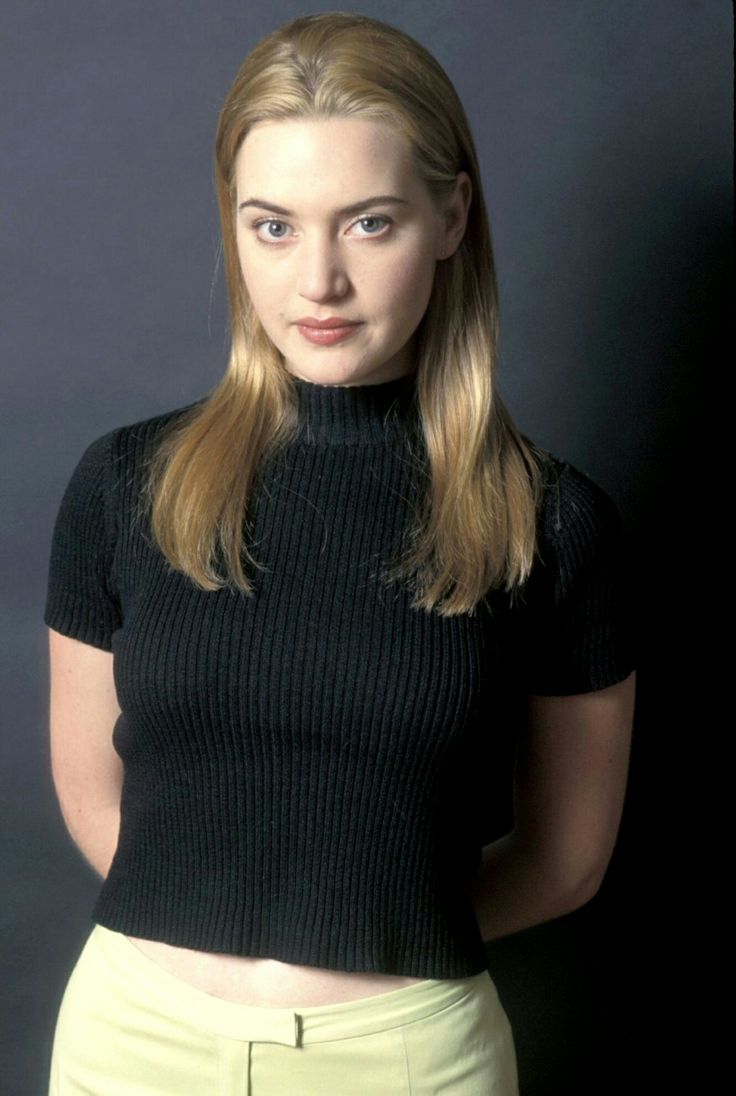 a woman with long blonde hair wearing a black shirt and yellow pants poses for a photo