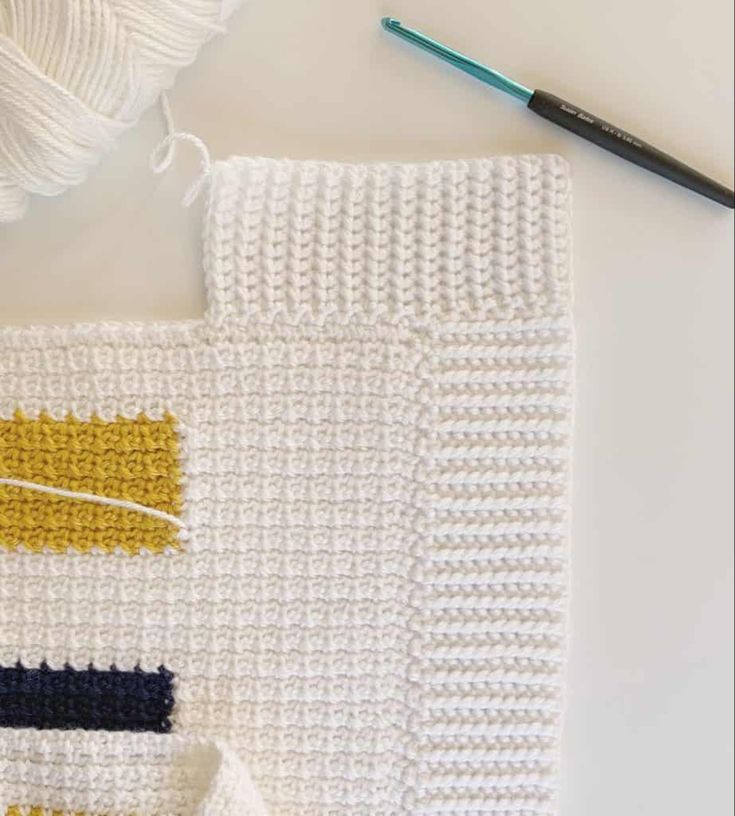 a crochet project with yarn and scissors on the table next to it is a white knitted blanket