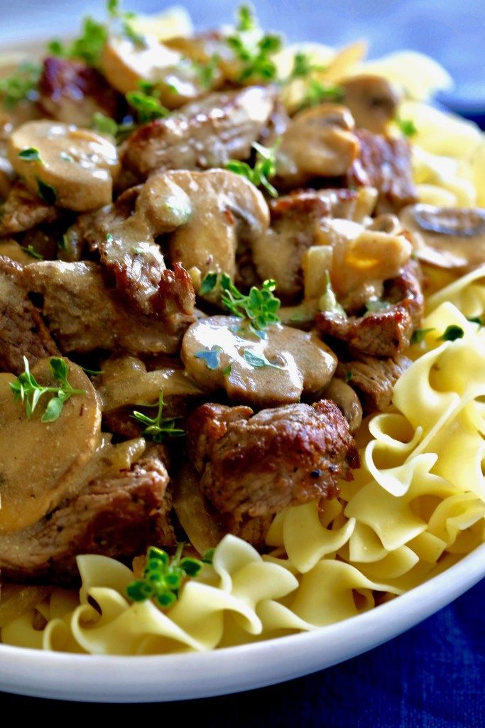 a white plate topped with pasta and meat covered in mushroom sauce on top of a blue table cloth