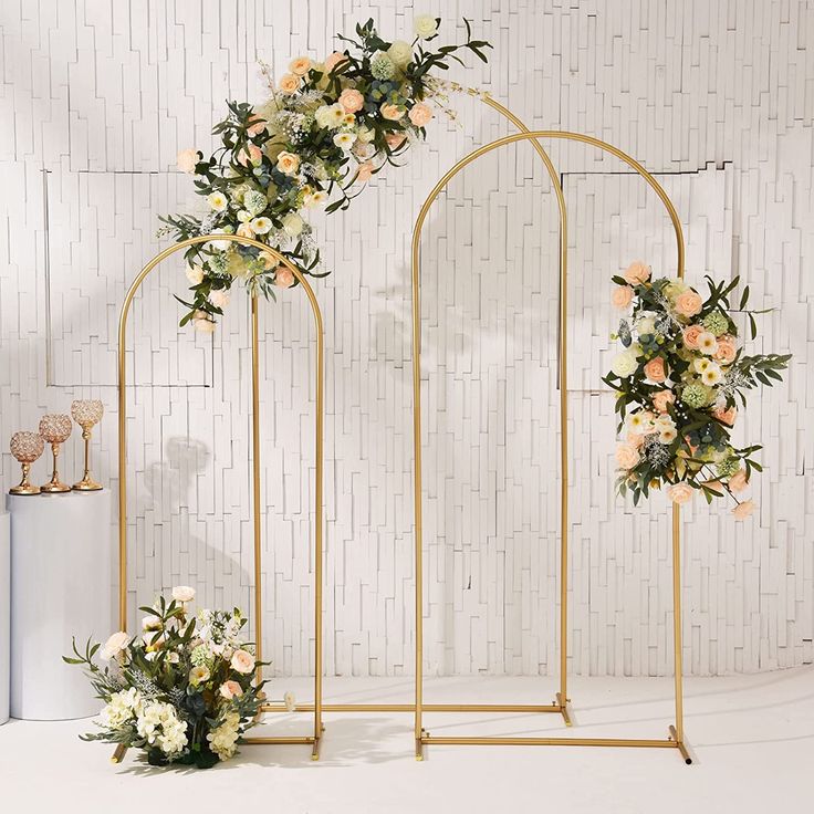 an arch decorated with flowers and greenery next to two vases on the floor