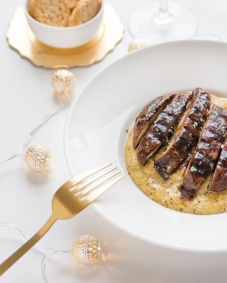 a white plate topped with meat and grits next to a bowl of crackers