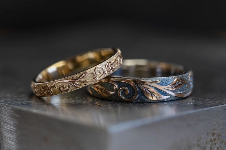 two gold and silver wedding bands sitting on top of a metal table next to each other