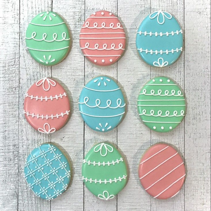 decorated cookies are arranged in rows on a white table with wood planks behind them