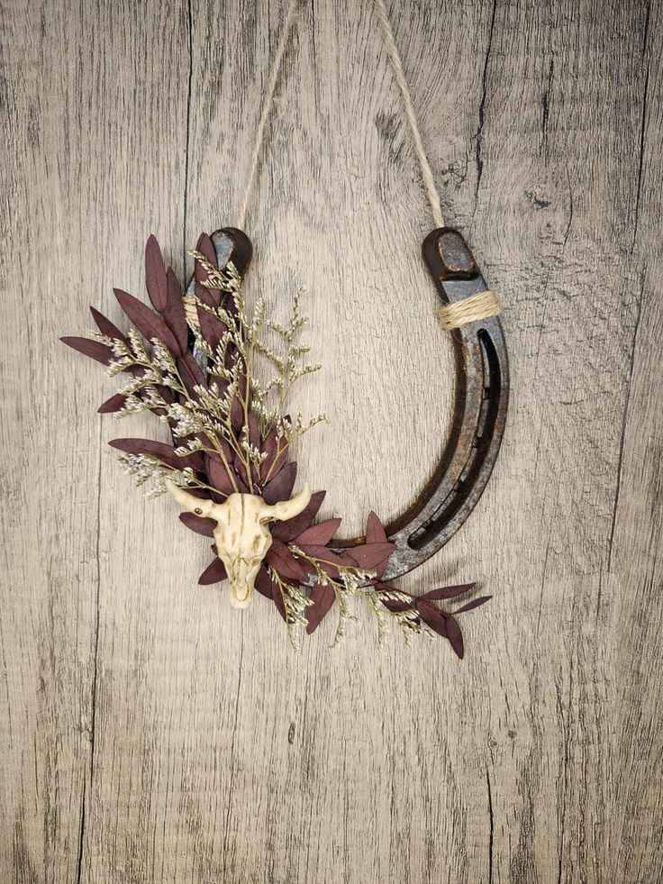 an animal's skull hangs on a wooden wall with dried flowers and leaves in the foreground